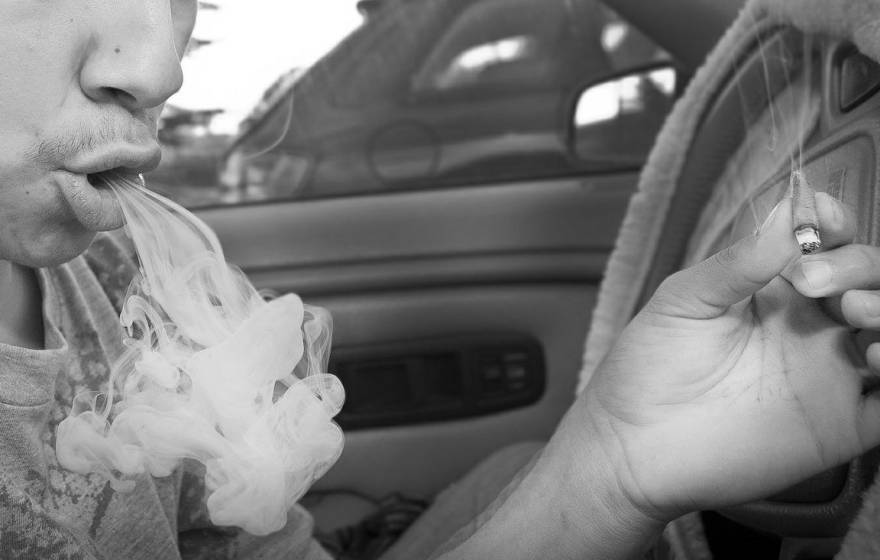A man behind the wheel of a car exhales a big puff of smoke