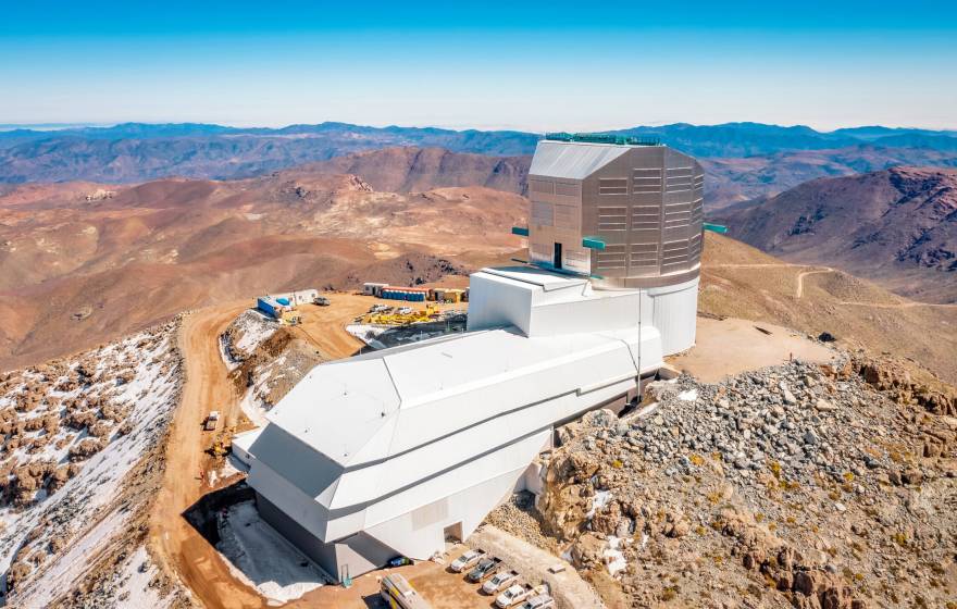 A huge, modern building atop a remote, snow-covered mountain, with desolate mountains stretching into the distance