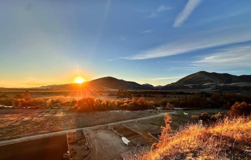 Sunrise over rolling hills, casting warm light on the landscape and clear blue sky.