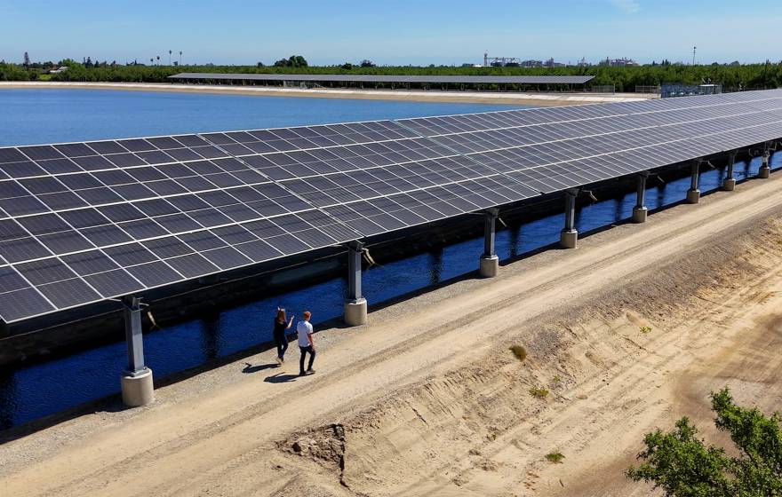 Two people walk next to a long set of solar panels over a canal