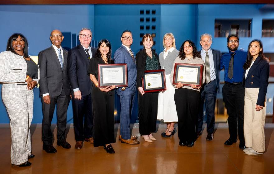 About ten people pose for a photo wearing business attire, three holding plaques.