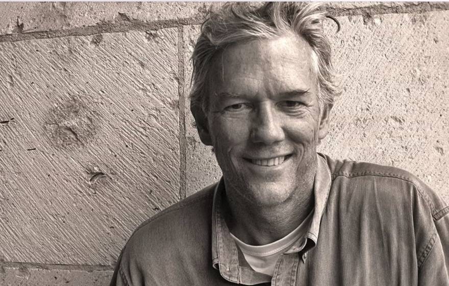 William Finnegan smiles against a brick wall in a sepia-tinted image
