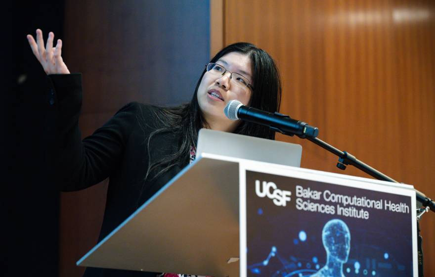 A young woman points at a screen off-camera while at a UCSF lectern
