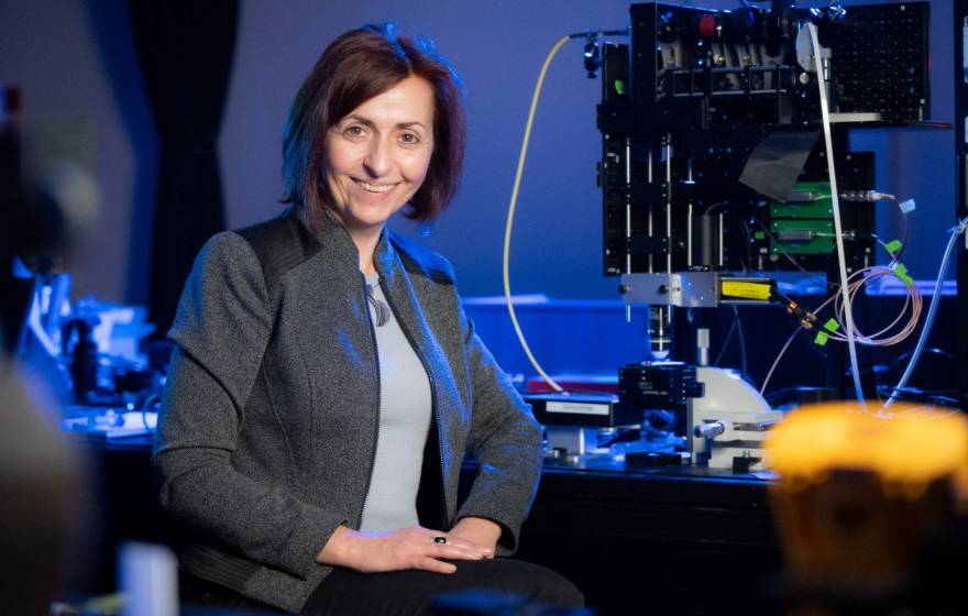 A woman smiles in front of a piece of equipment in a lab