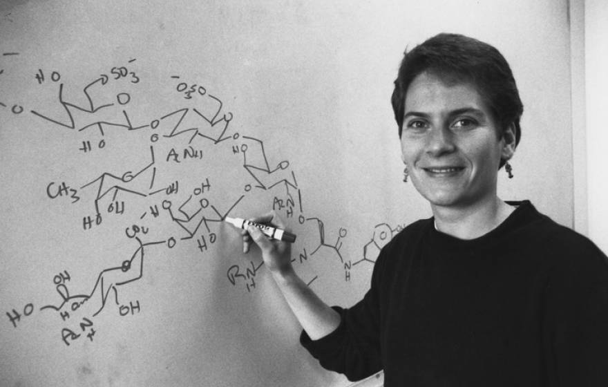 Black and white photo of Carolyn Bertozzi at a chalkboard