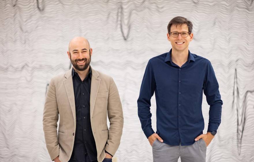 Two men standing together in front of a backdrop of wavy lines
