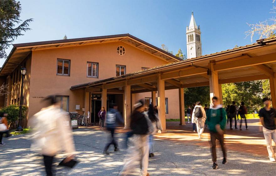 Students walk in front of the music building on Cal's campus, with the campanile in the background
