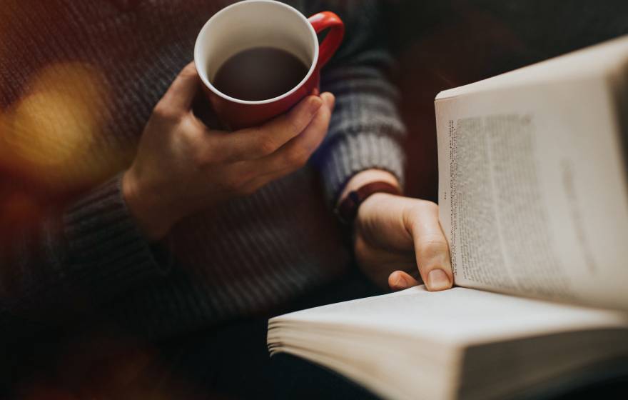 A view of someone holding a cup of coffee and reading a book from above