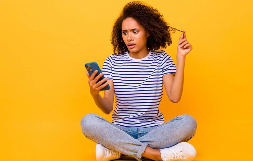 A woman looking at a smartphone with a shocked and worried expression