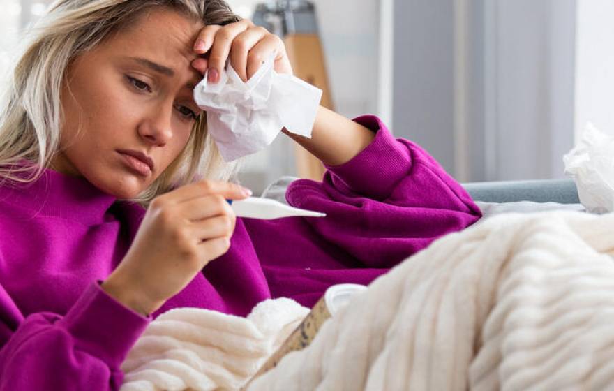 Woman sitting on a couch looking a thermometer