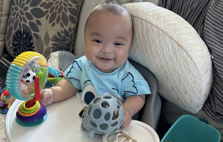 A baby smiles at the camera and plays with toys in a bouncy seat