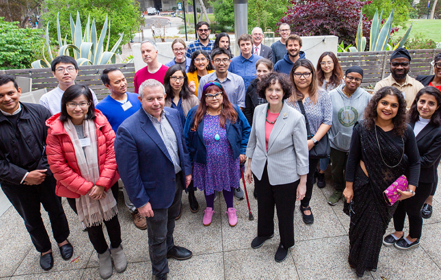 A group of people stand on a patio with lots of plants smiling for a group photo