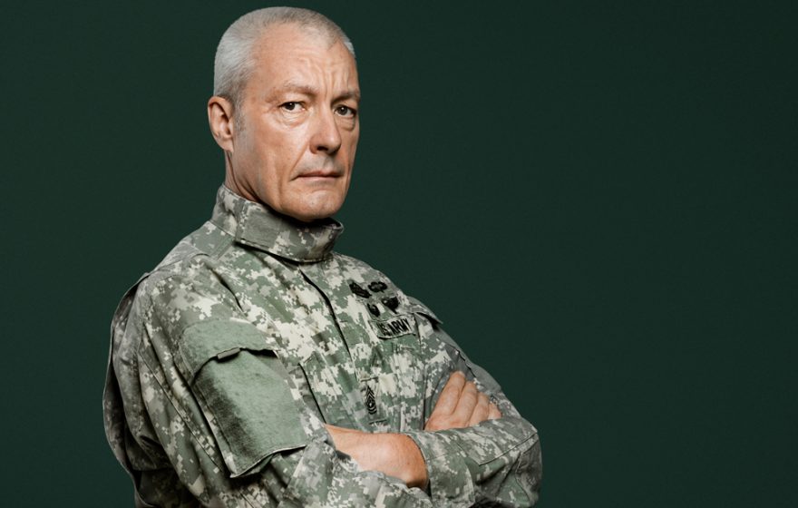 A man in military uniform stands with his arms folded across his chest.