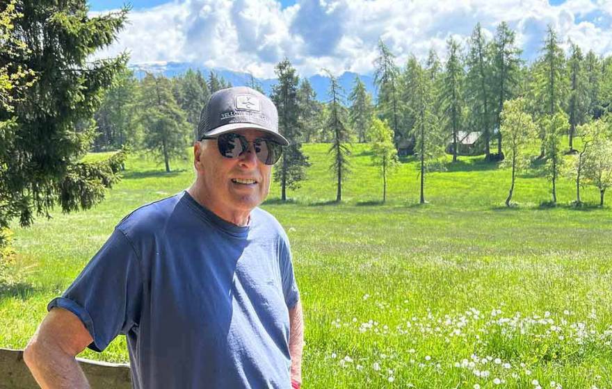 A man wearing a ballcap stands in the Sierras on a beautiful day