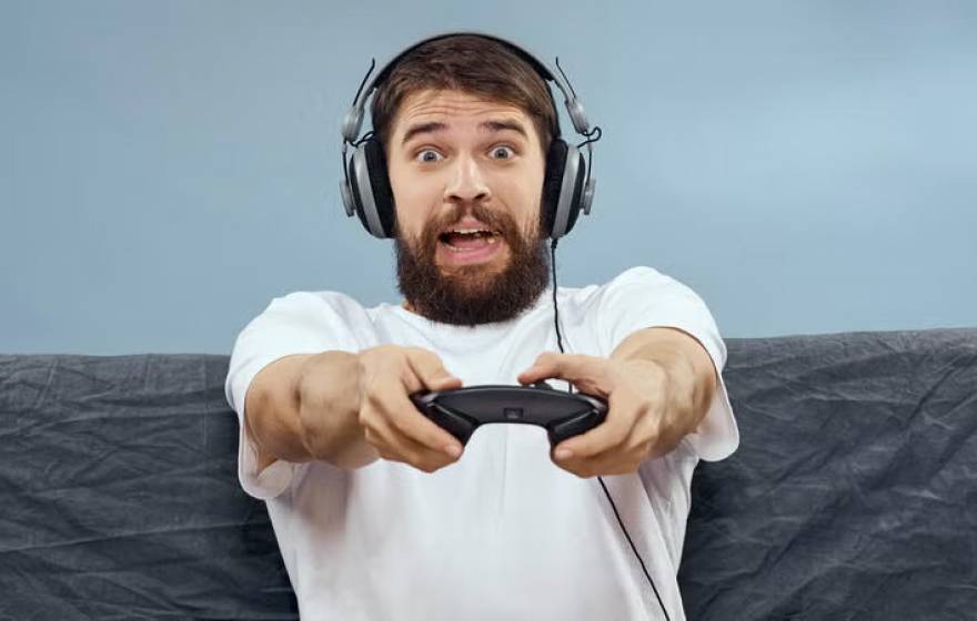 A man sitting on a couch with headphones on holding a video game controller with a surprised, frightened expression
