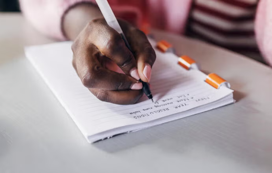 A close-up of a hand holding a pen writing a list in a notebook