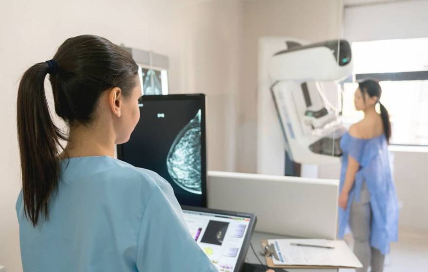 Nurse and patient conducting a mammogram, patient in front of machine