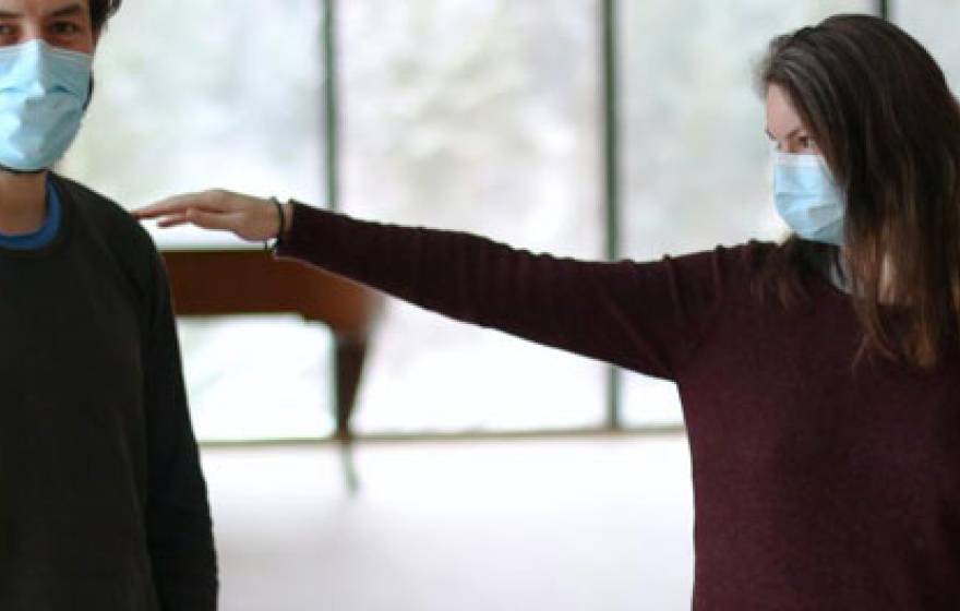 A young man and a woman wearing masks, woman reaching out to man with arm