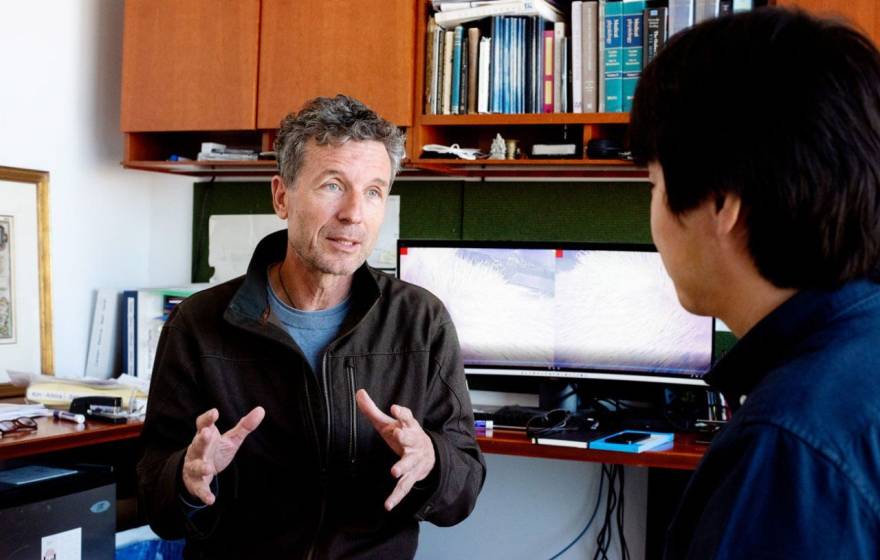 A researcher with gray hair at his desk talks to someone
