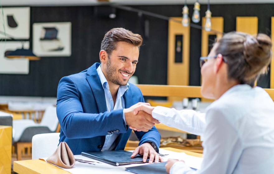 Man smiling and shaking the hand of a woman over a table