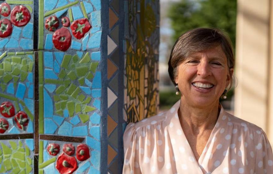 Woman smiles next to an outdoor pillar with a tomato mosaic