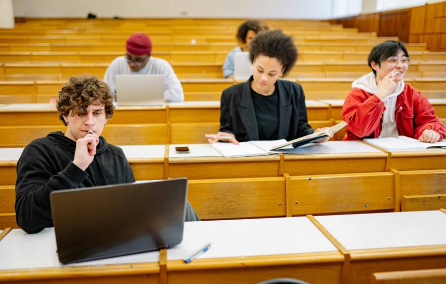 Five students in four rows of a lecture hall work independently