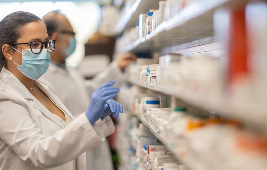A pharmacist in a face mask reaching for drugs