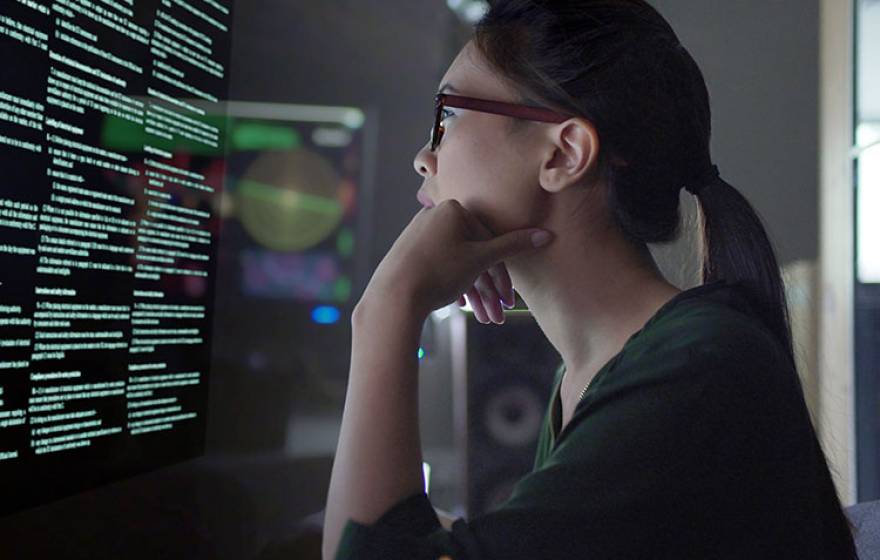 Young Asian woman looking at code on a screen in a dark room