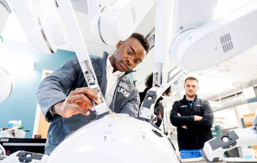 A student focuses intently as he operates one arm of a many-armed robot, while a teacher watches