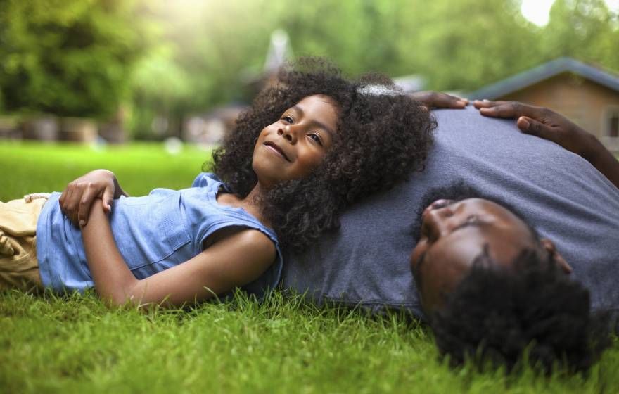 A young girl reclines against her father's shoulder on fresh grass