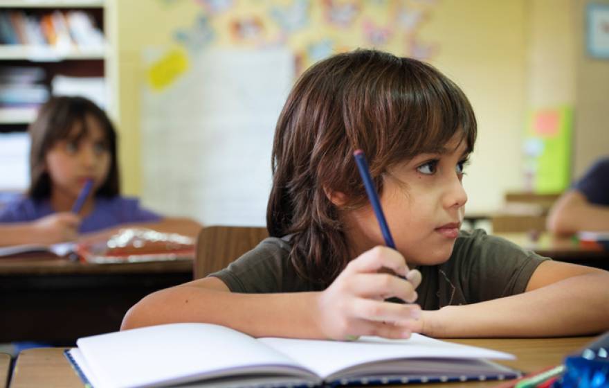 Boy looking up in a classroom, pencil in workbook