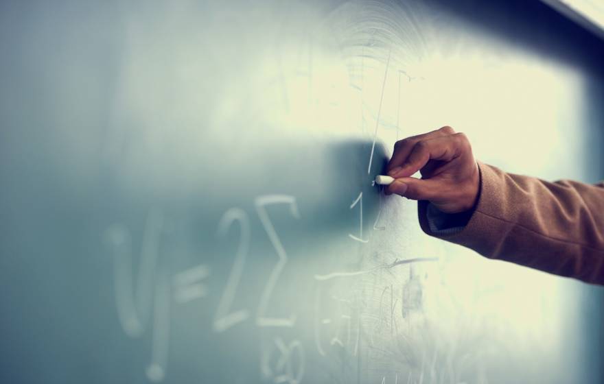 A Black teacher writing on a chalkboard