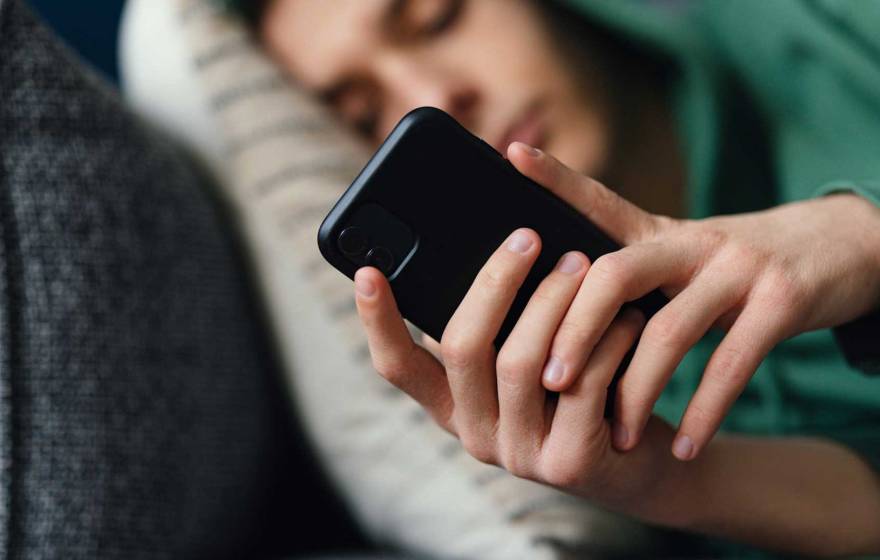 A teen, slightly out of focus, lying on the couch, looking at phone