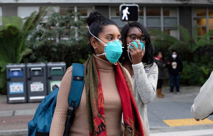 Two Black women wearing masks cross the street