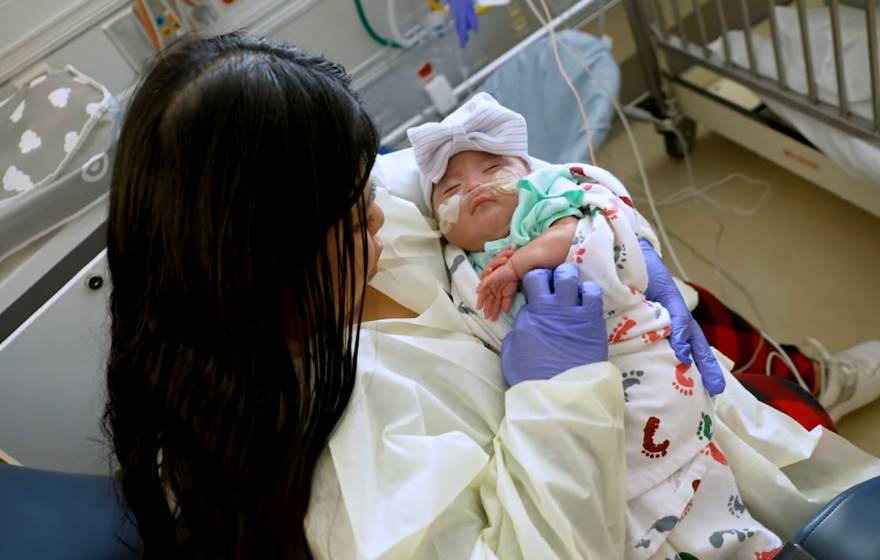 A young woman holds a young baby in her lap at a hospital