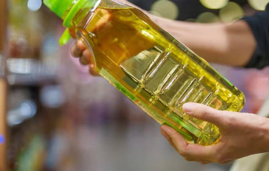 A pair of hands hold a bottle of soybean oil at an angle