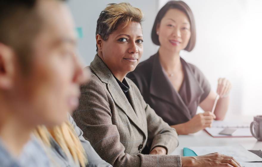 Middle-aged Black woman and middle-aged Asian woman look at a younger man in the office who is closer to the camera