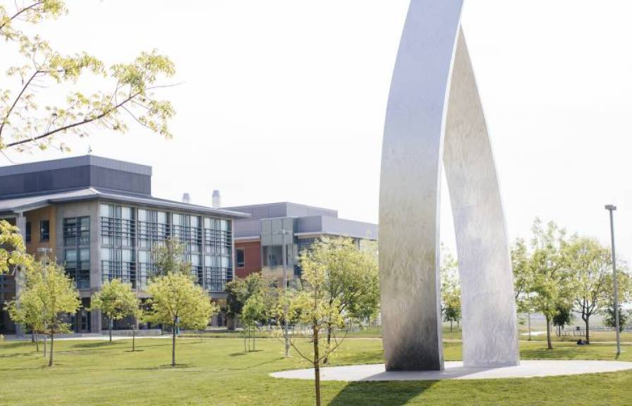 Silver sculpture on a large lawn with buildings in the background at UC Merced.