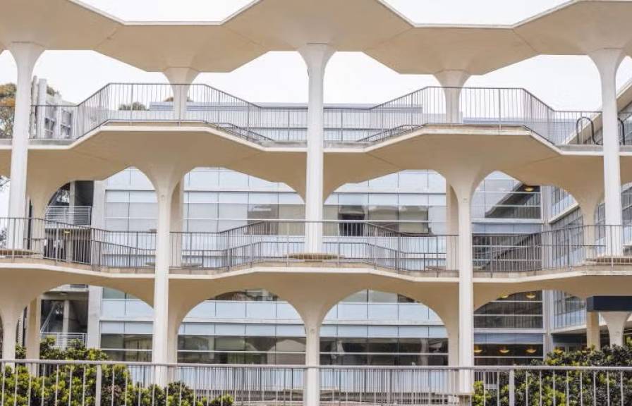 White structure with walkways and a glass building behind it.