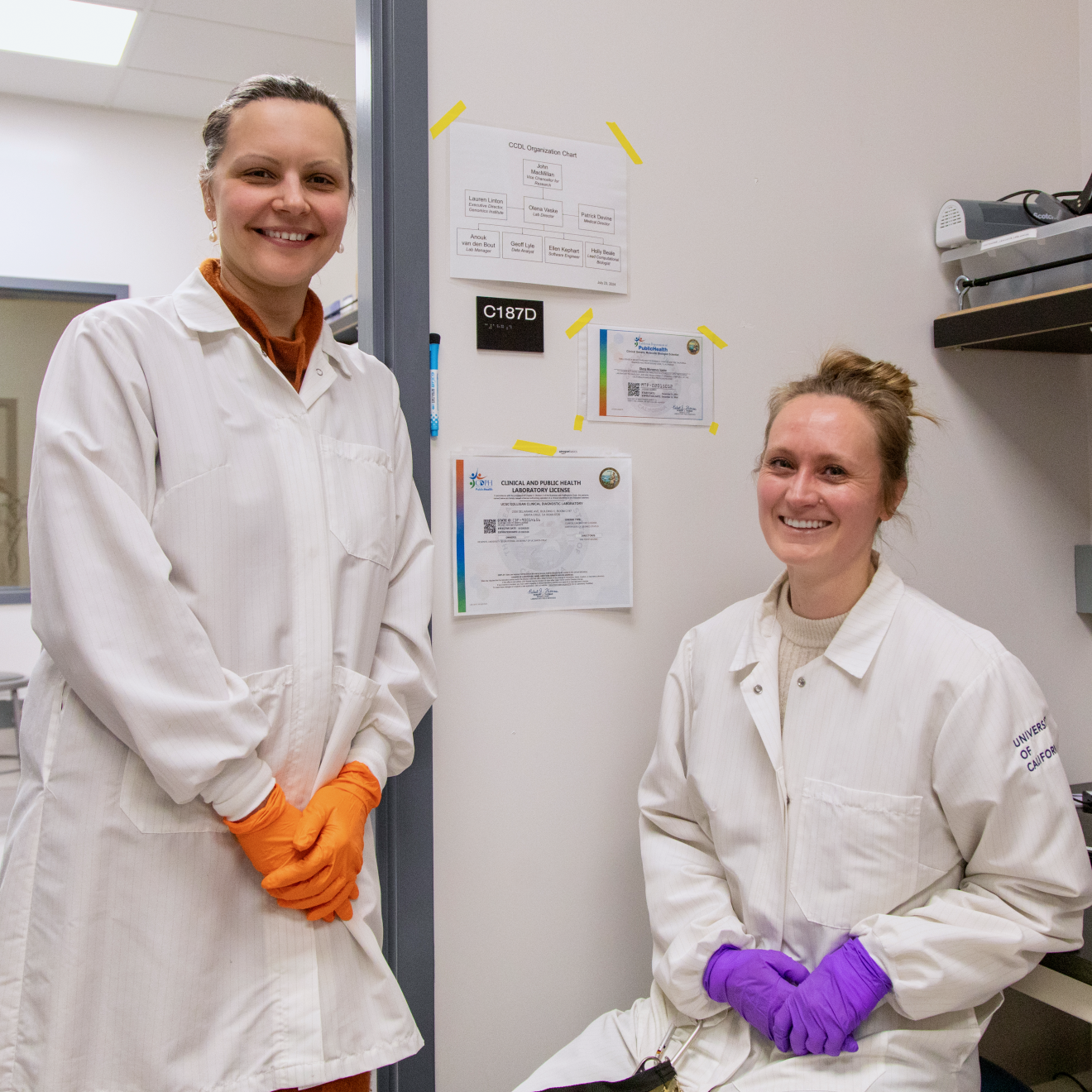Two researchers wearing lab coats and brightly colored gloves