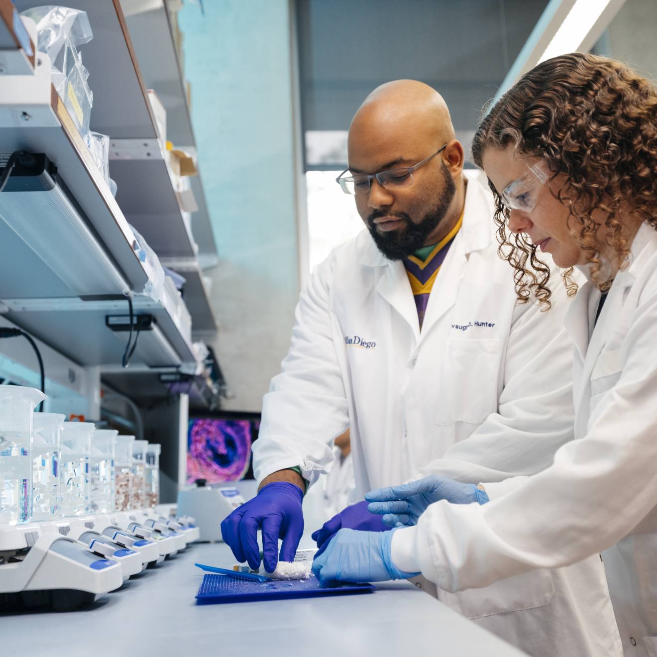 Two scientists in white lab coats work together in a laboratory.