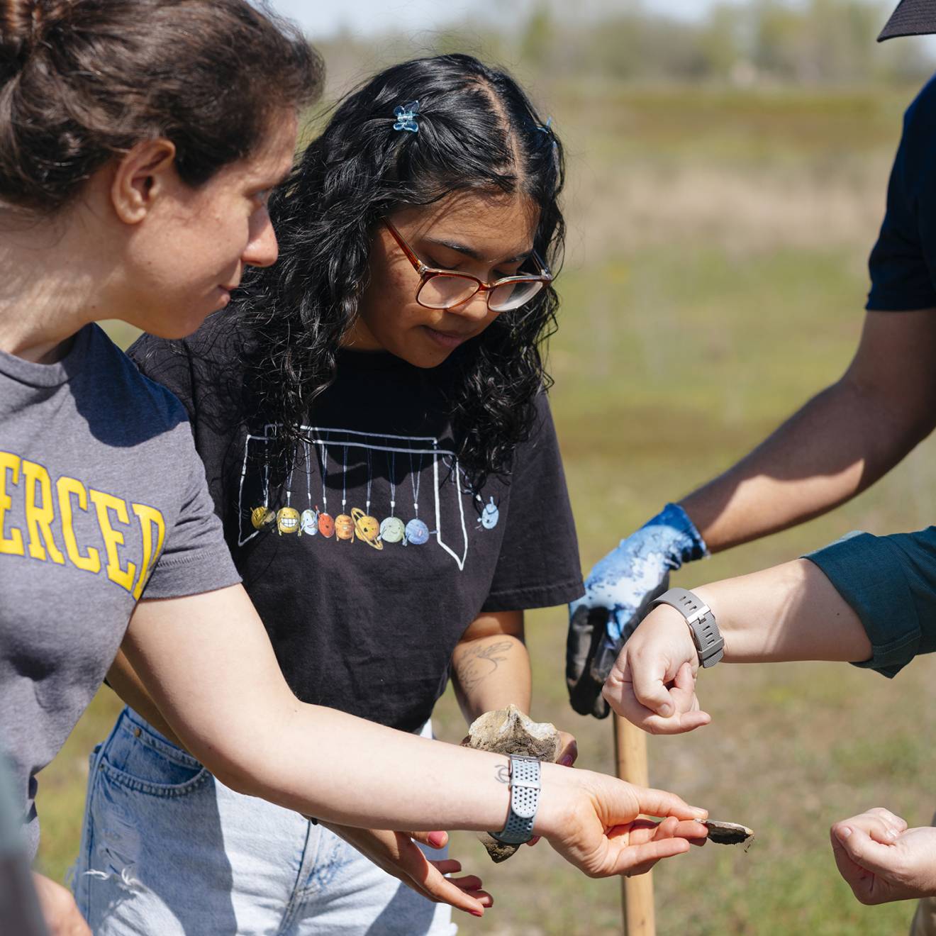 A group of people in a field, one is holding a rock they are all looking at