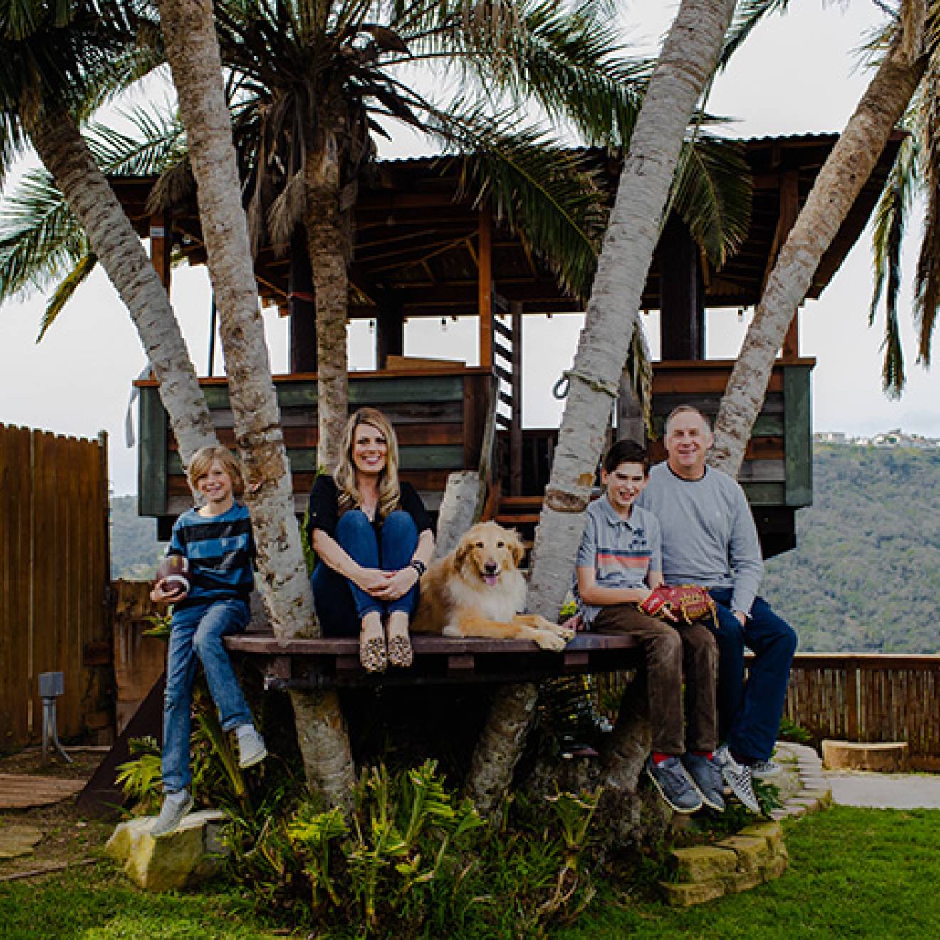 A family of four, with a golden retriever, sits together in a treehouse