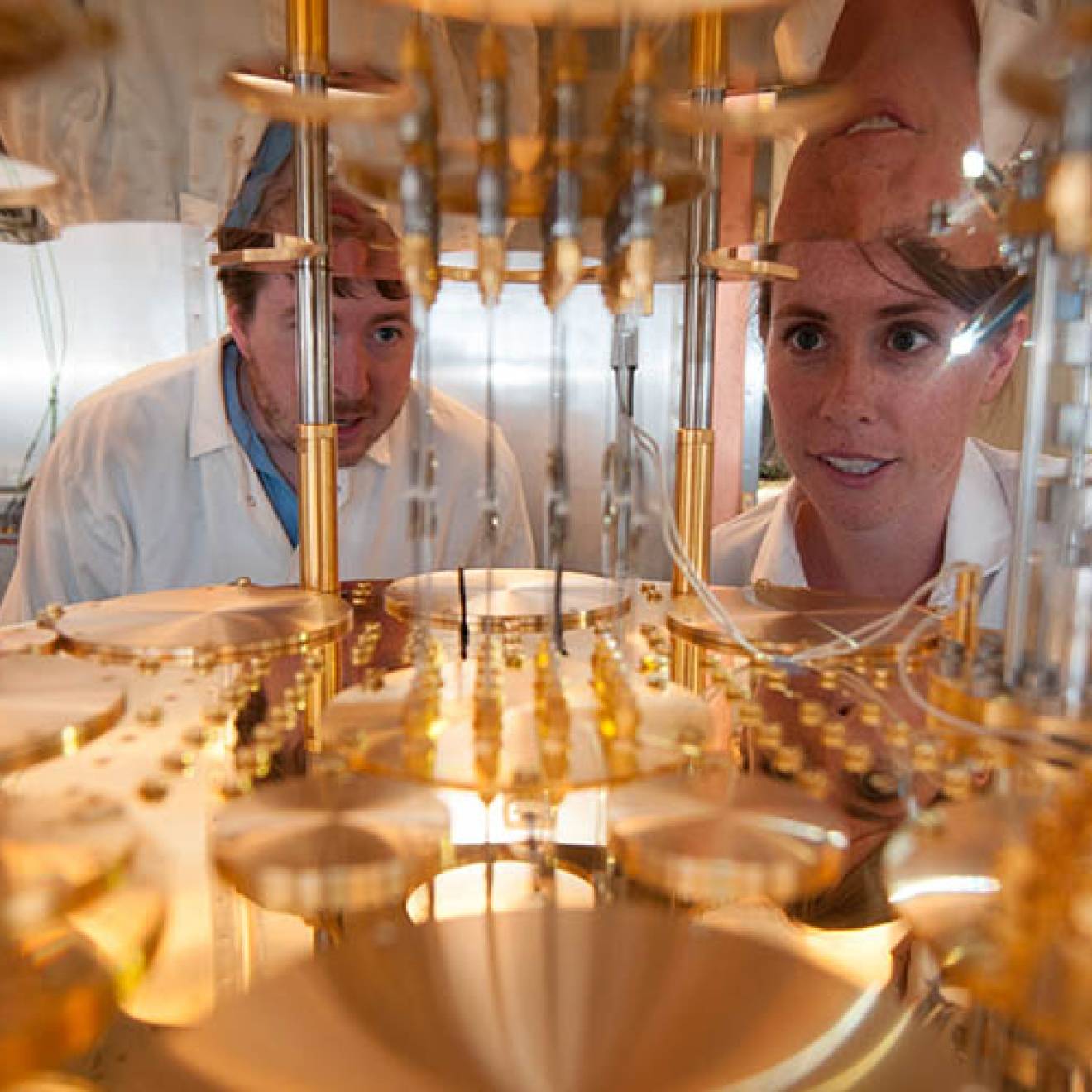Three people in white lab coats peer into a very large, delicate, gold-colored machine.