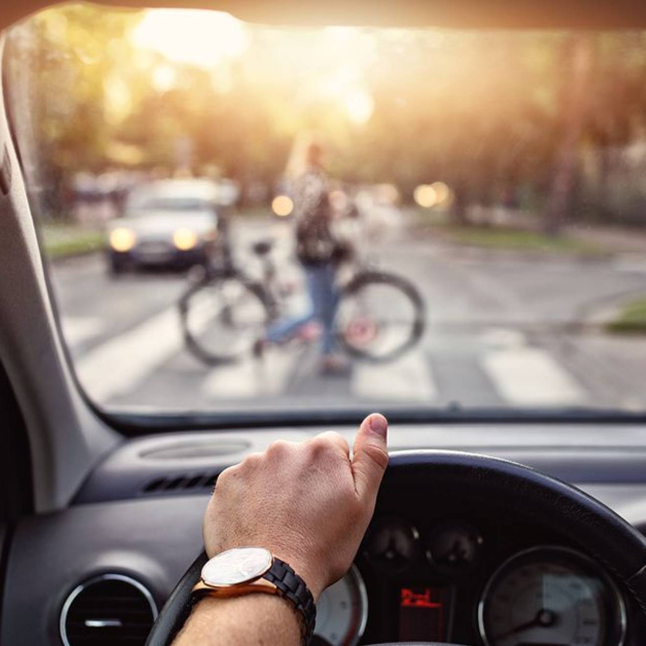 A view of someone's hand on a steering wheel and a person walking a bicycle across the crosswalk out of focus