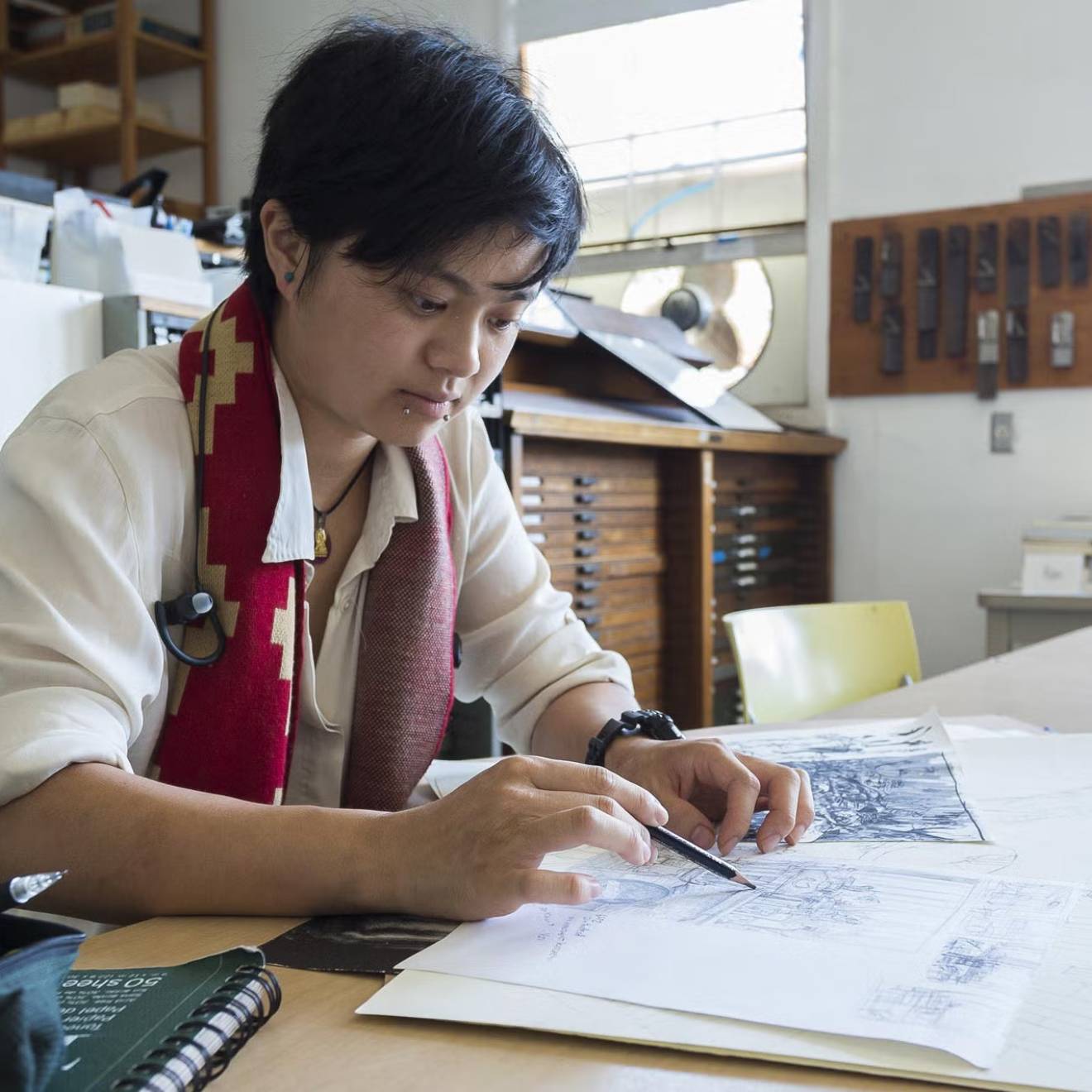 A student in an art studio holds a pencil over a sketchbook