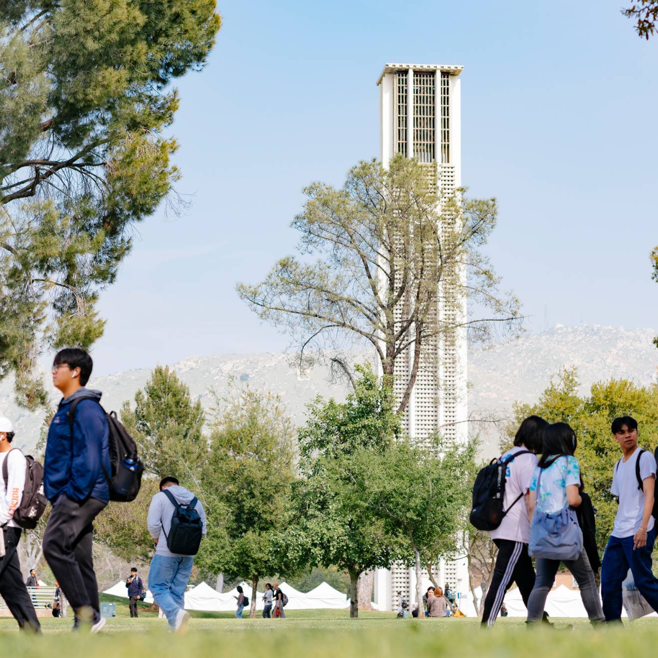 The UC Riverside Bell Tower seen through trees across campus, with students walking in the foreground