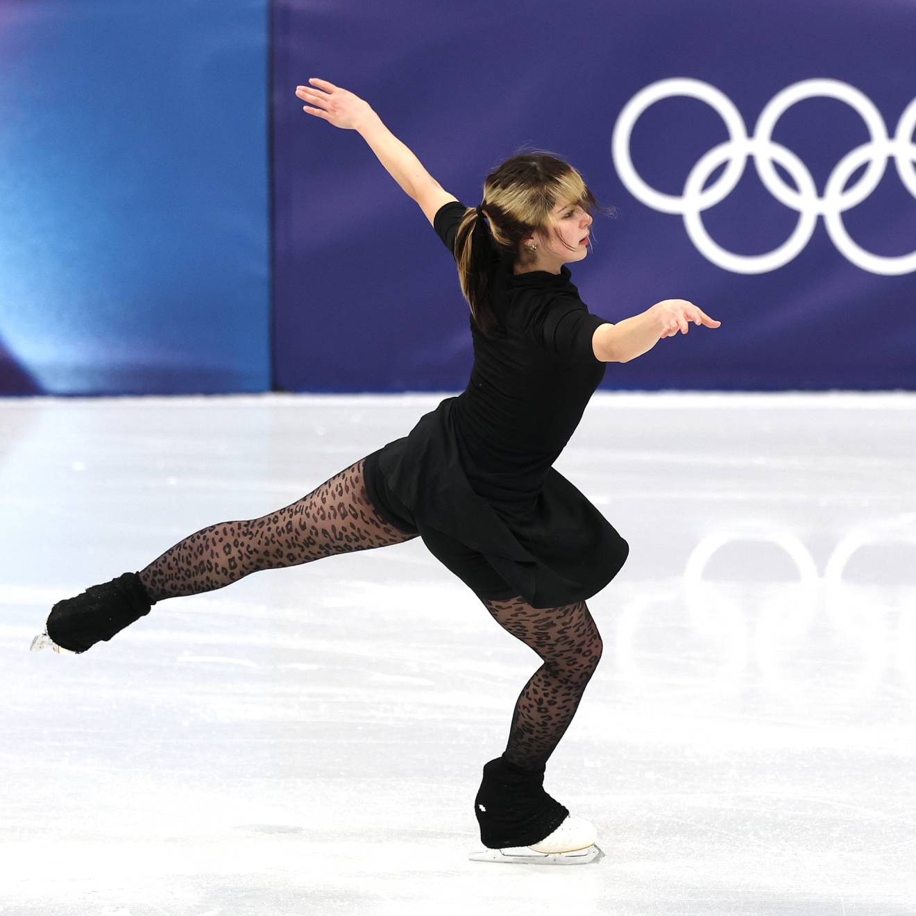 A figure-skating woman woman stretches her arms and back leg while practicing on the ice
