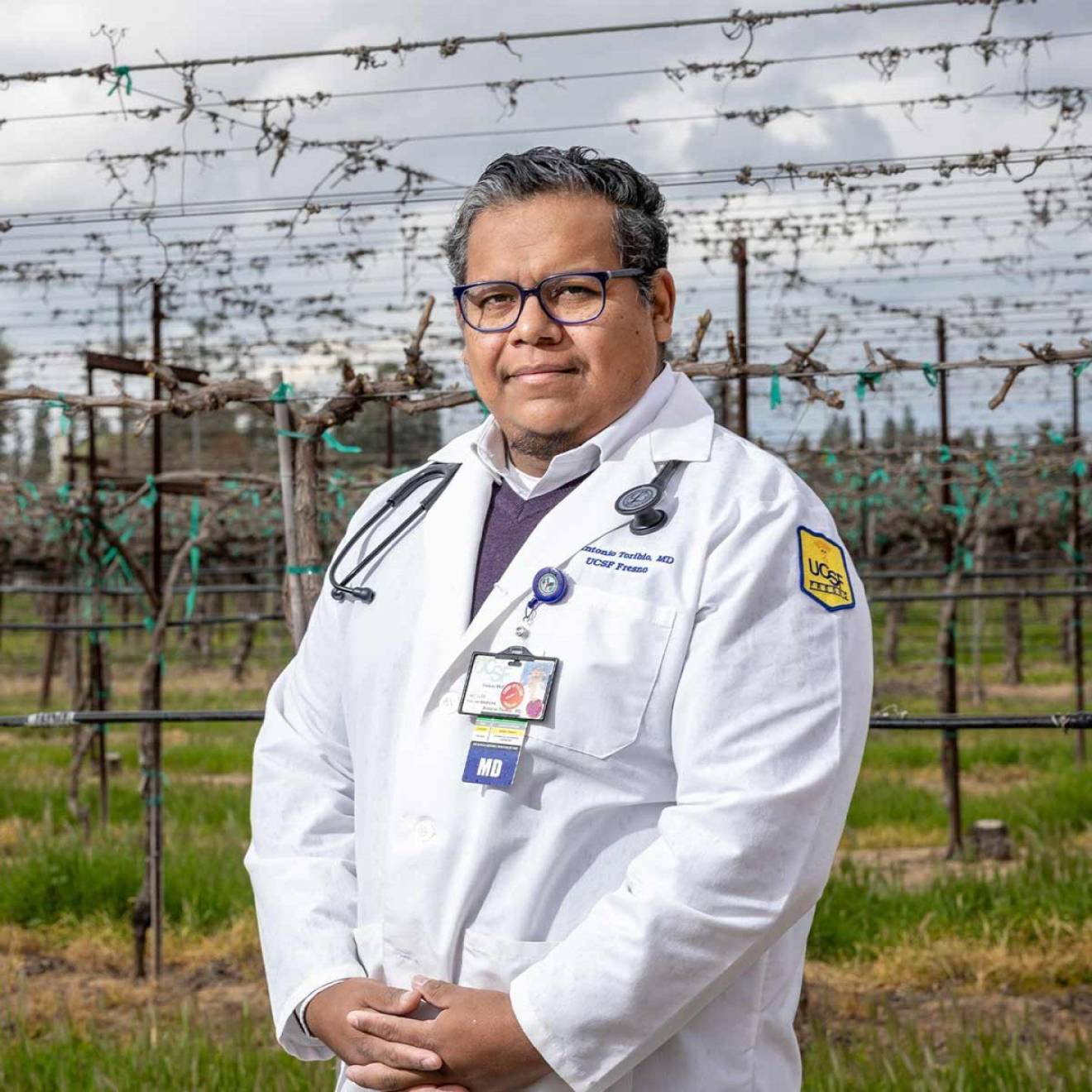 Doctor with dark gray hair and a medical coat stands in front of a vineyard