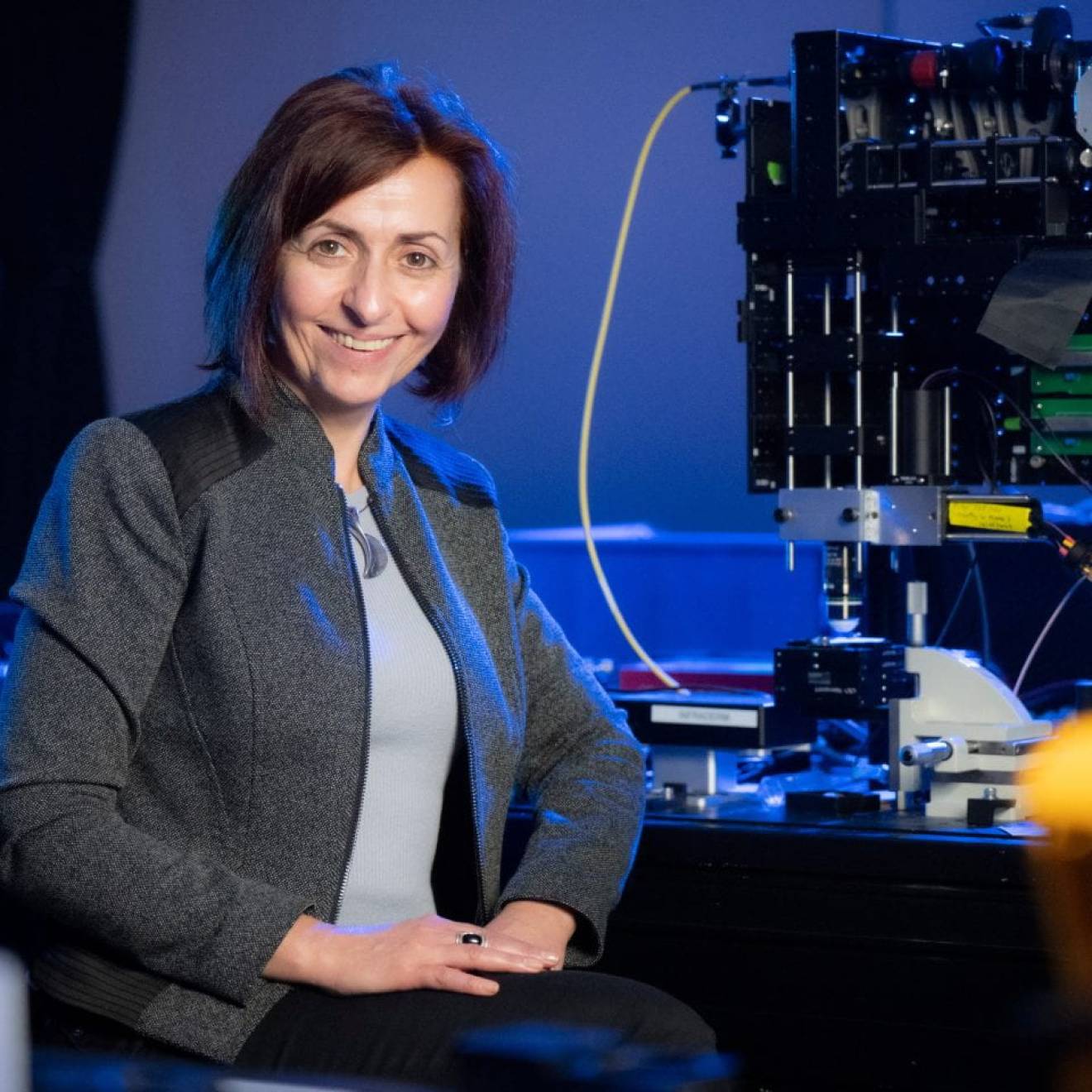 A woman smiles in front of a piece of equipment in a lab